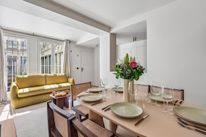 A dining area with a table set for four, a sofa, and a vase of flowers. - Lavie Maison – Hot Tub & AC – Central Paris (Paris)