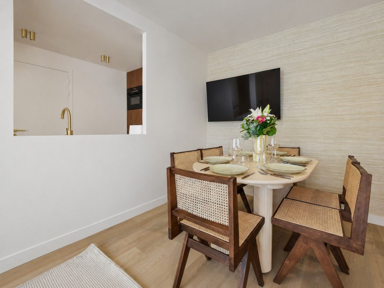 Un coin repas avec une table ronde, quatre chaises, un téléviseur à écran plat fixé au mur et un petit vase avec des fleurs.