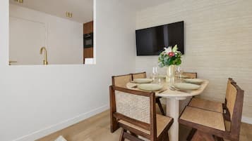 Un coin repas avec une table ronde, quatre chaises, un téléviseur à écran plat fixé au mur et un petit vase avec des fleurs.