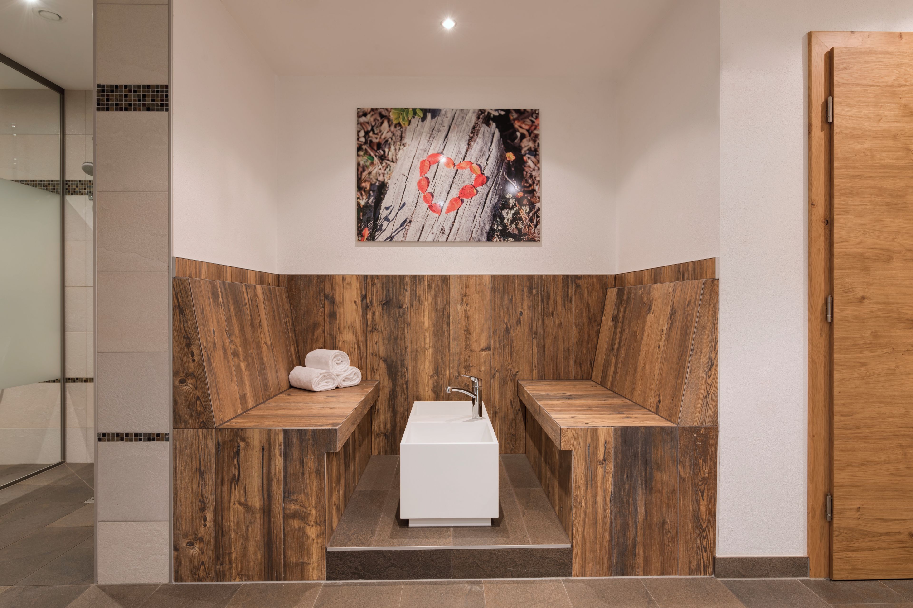 Un baño con paneles de madera, un lavamanos blanco y una obra de arte con forma de corazón en la pared.