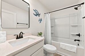 Et badeværelse med vask, spejl, toilet, brusebad og dekorativ vægkunst.