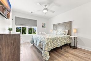Une chambre à coucher avec un lit, un ventilateur de plafond, une fenêtre donnant sur un beau paysage et une table de chevet avec une lampe.