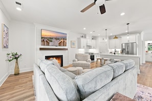 A modern living room with a large grey sectional sofa, a fireplace, and a flat-screen TV mounted above it. - Choose Happiness Updated 4 BR short golf cart ride Pawleys Pet Friendly (Pawleys Island)