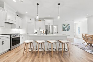 Une cuisine moderne avec des meubles blancs, un îlot central doté de tabourets, des appareils en acier inoxydable et un éclairage suspendu.