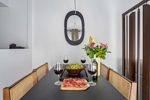 A dining table with a bowl of grapes, a bottle of wine, and a glass of wine. There is a vase with flowers and a mirror on the wall.