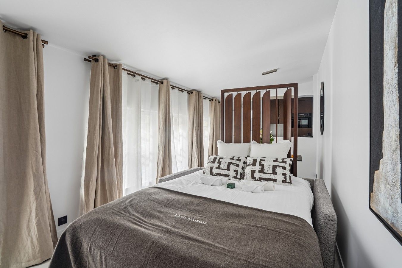 Ein Hotelzimmer mit Bett, Vorhängen, einem Kopfteil, einem Wandbild und einem Nachttisch.