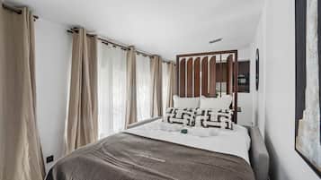 Ein Hotelzimmer mit Bett, Vorhängen, einem Kopfteil, einem Wandbild und einem Nachttisch.