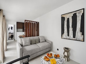 A living room with a sofa, a coffee table with pastries, a painting, and a kitchen in the background.