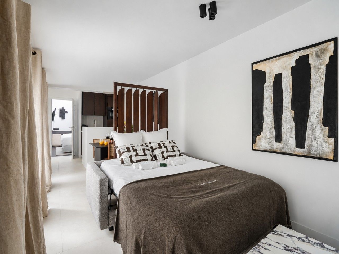 Een hotelkamer met een bed, een bureau, een stoel en een groot abstract schilderij aan de muur.