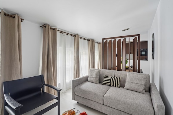 A modern living room with a sofa, a black chair, and a dining table with a plate of pastries.
