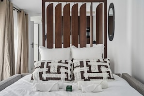 A bed with white linens, two patterned pillows, and a green bottle on the side.