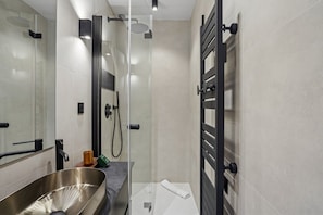 A modern bathroom with a glass-enclosed shower, a stainless steel sink, and a towel rack.