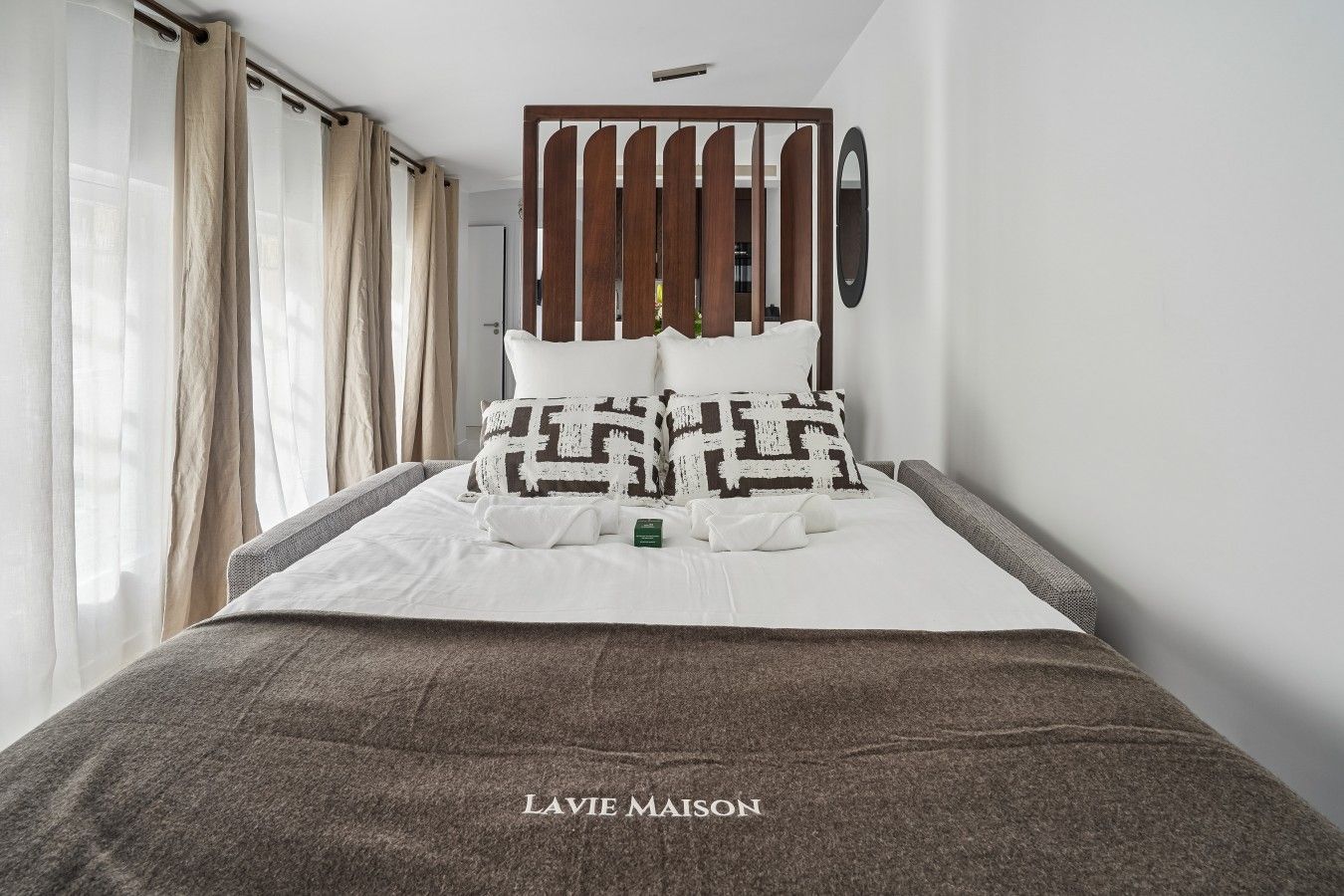 Une chambre d’hôtel avec un lit, une cloison en bois, un miroir et une fenêtre avec des rideaux.