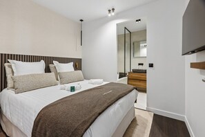 A modern hotel room with a large bed, a bedside table, a mirror, and a TV mounted on the wall.