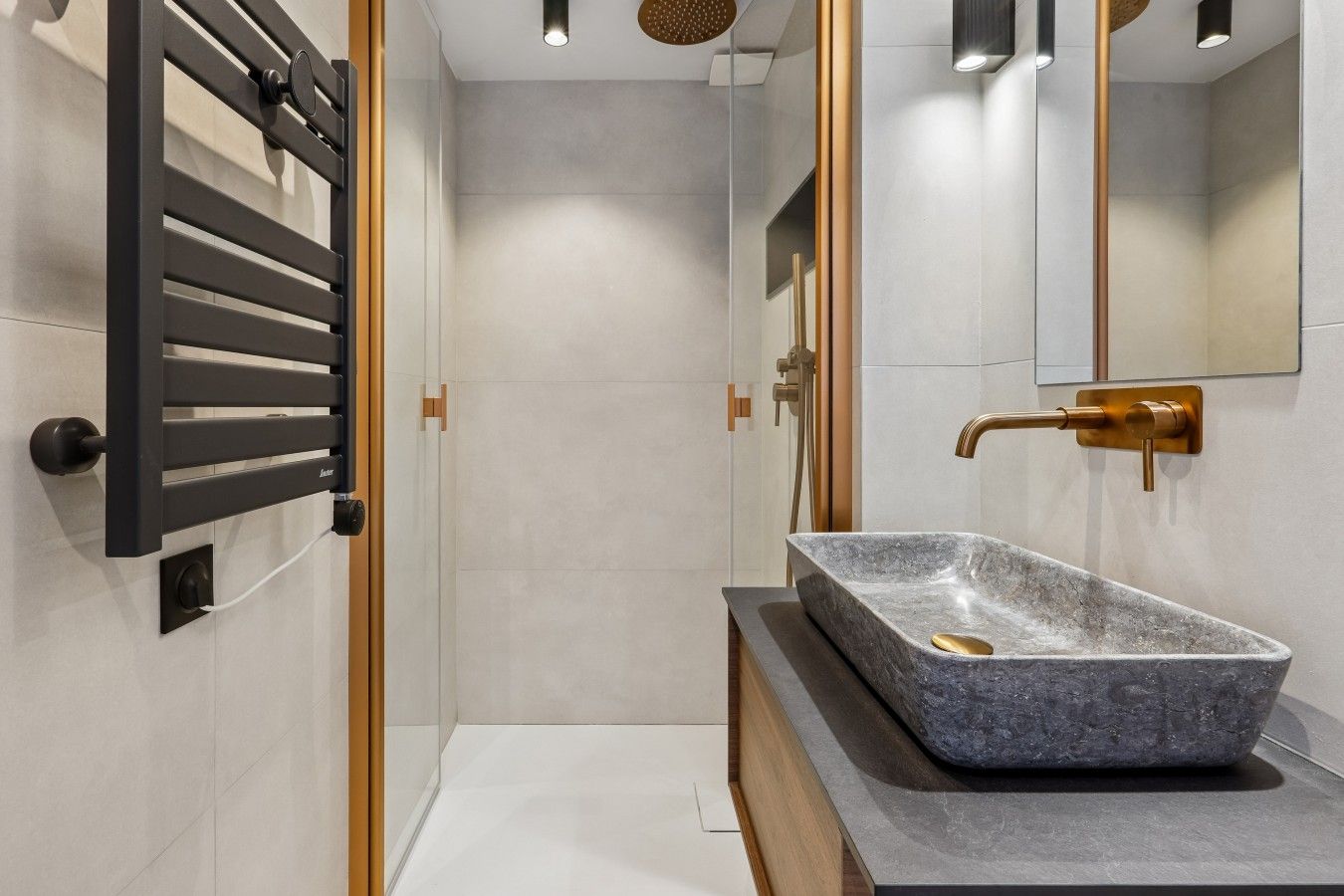 Une salle de bain moderne avec un lavabo rectangulaire en pierre, un robinet doré et un porte-serviettes noir.