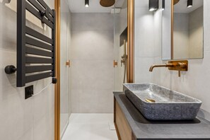 A modern bathroom with a rectangular stone sink, a gold faucet, and a black towel rack.
