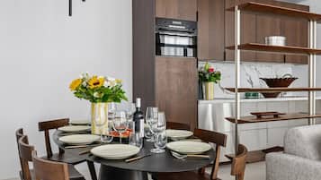 Un espace repas moderne avec une table ronde dressée pour six personnes, entourée de chaises en bois. Un vase rempli de fleurs jaunes est posé sur la table, ainsi que des verres à vin et une bouteille de vin.