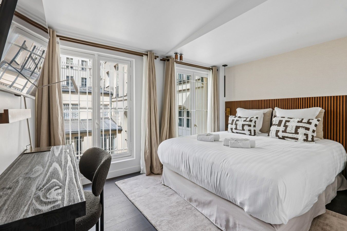 Een hotelkamer met een bed, een bureau, een stoel en uitzicht op gebouwen door het raam.