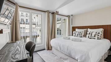 Een hotelkamer met een bed, een bureau, een stoel en uitzicht op gebouwen door het raam.