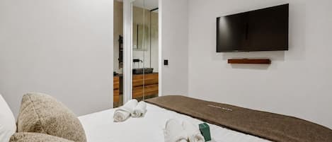 A hotel room with a bed, a flat-screen TV mounted on the wall, and a mirror reflecting the room.