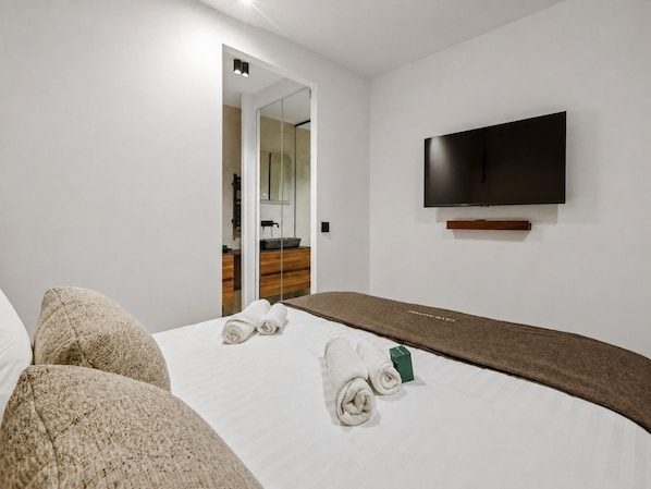 Une chambre d’hôtel avec un lit, un téléviseur à écran plat fixé au mur et un miroir qui reflète la pièce.