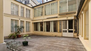 Ein Innenhof mit einem Gebäude, das große Fenster, eine Tür und einen Fahrradständer aus Metall zeigt.