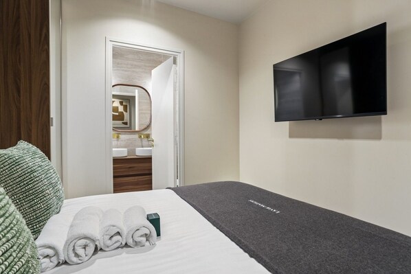 A hotel room with a bed, a TV, a bathroom with a mirror, and a green and white patterned pillow.