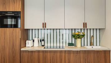 Une cuisine moderne avec des meubles en bois, un four en acier inoxydable, un plan de travail blanc, un évier avec un robinet doré et un vase rempli de fleurs.