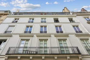 A multi-story building with a symmetrical facade, large windows, and a balcony with metal railings.