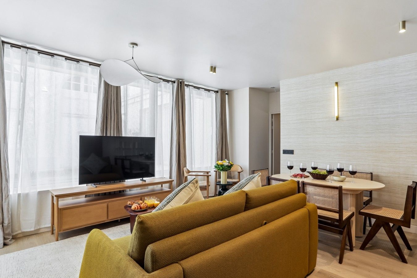 Een moderne woonkamer met een flatscreen televisie, bank, eettafel en stoelen.