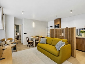 A modern living room with a sofa, a dining area, and a kitchen.