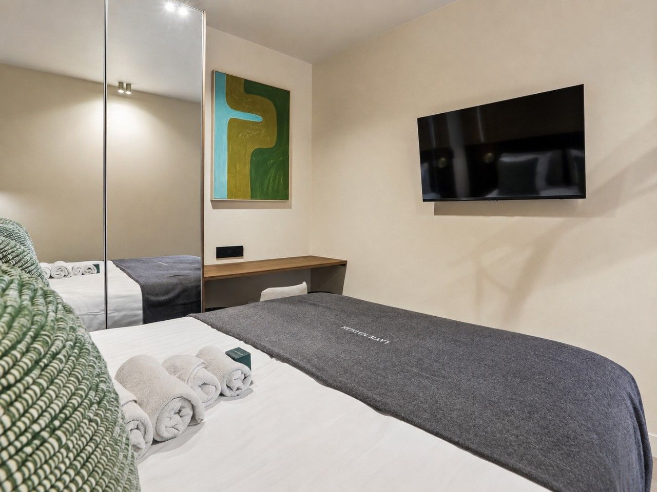 Une chambre d’hôtel avec un lit, un téléviseur à écran plat, un miroir et un tableau au mur.