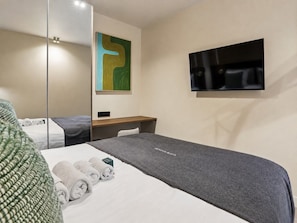 Habitación de hotel con cama, televisor de pantalla plana, espejo y un cuadro en la pared.