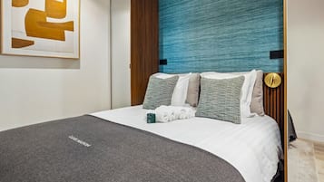 Un lit bien fait, avec une couverture grise, une tête de lit bleue à texture et plusieurs oreillers.