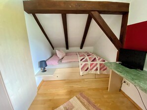 A small, cozy room with a sloped ceiling, a bed with pink bedding, a small table with a lamp, and a green countertop. - Bergulme Vacation Rental with a View of the Tyrolean Mountains (Mutters)