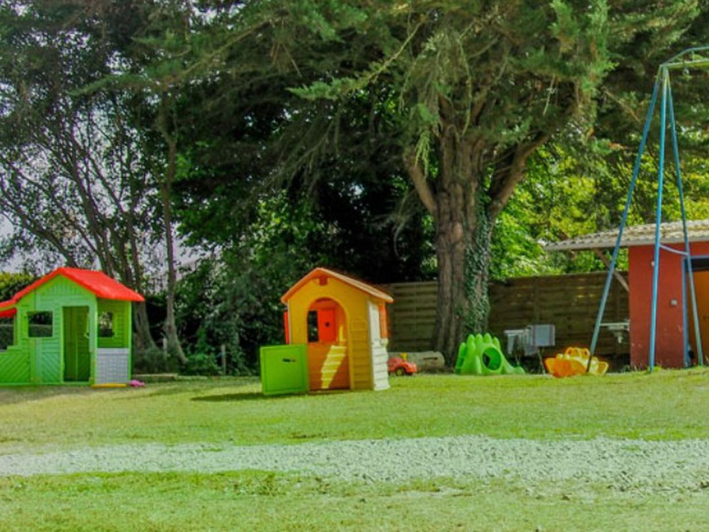 A grassy area with two small playhouses, one green and one orange, and a swing set.