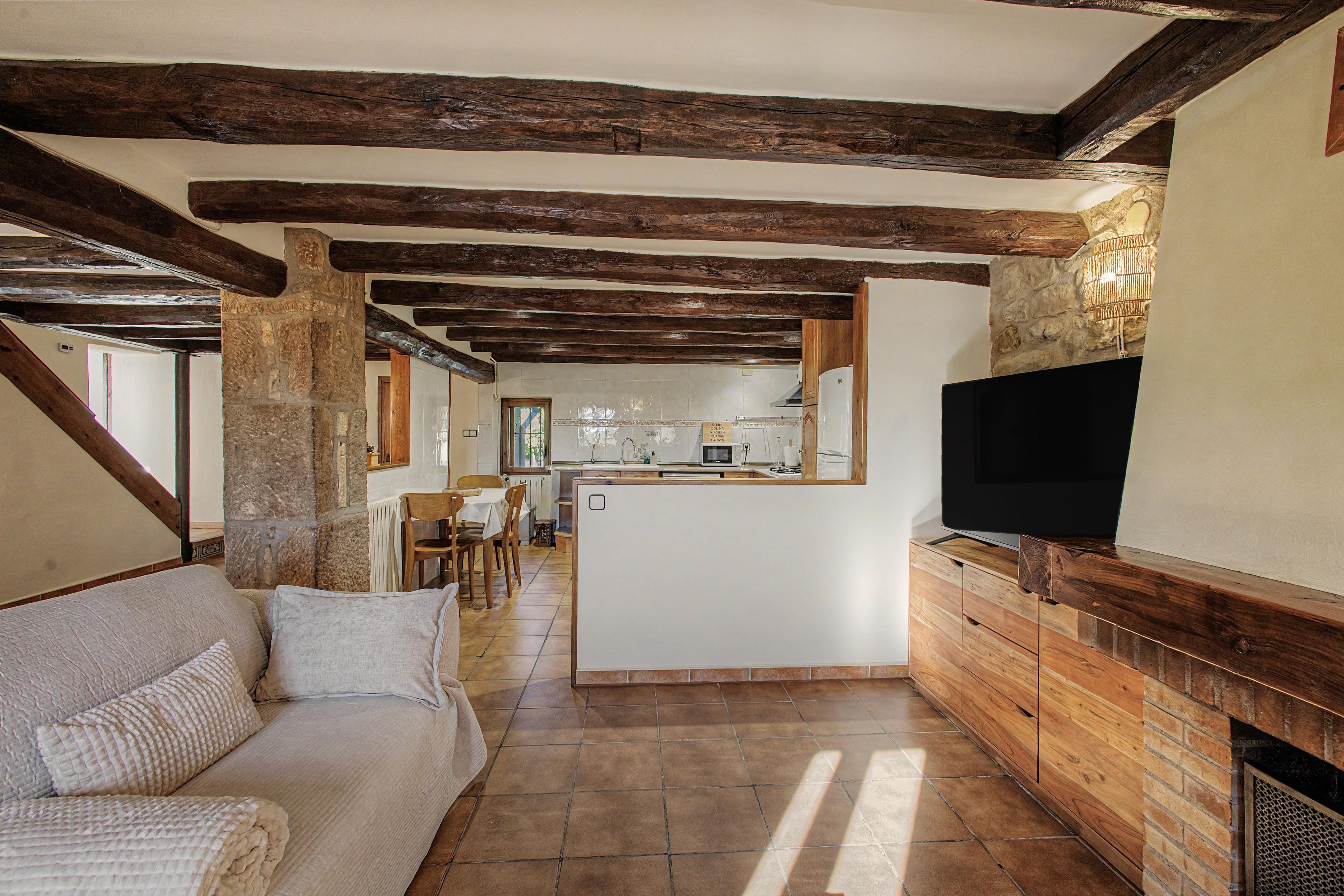 Una zona d'estar acollidora amb un sofà, un televisor de pantalla plana fixat a una paret de fusta, i una cuina al fons.
