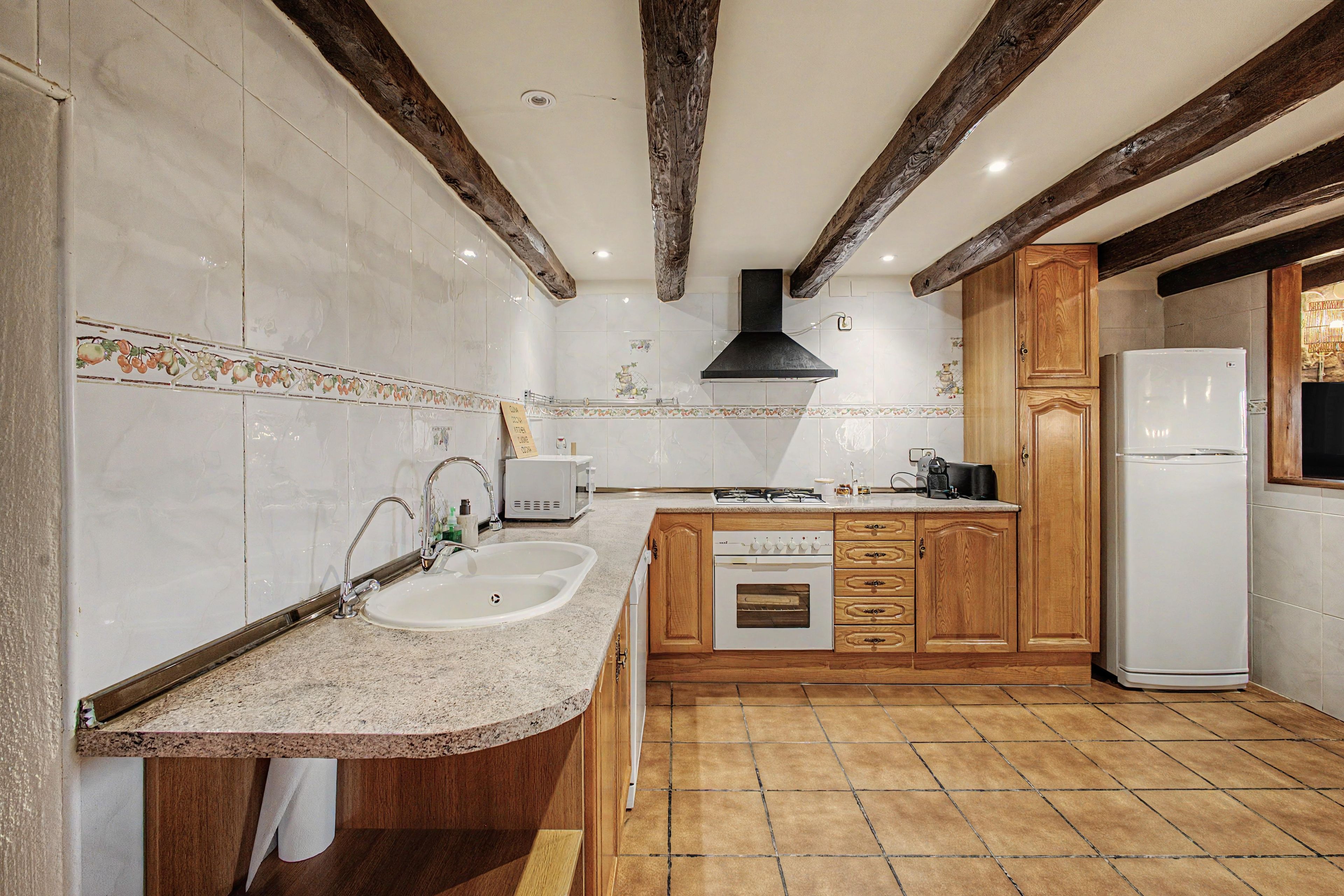 Una cocina con encimera de granito, pileta blanca, muebles de madera, horno empotrado y refrigerador blanco.