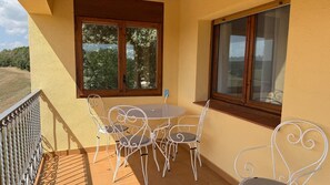 Un balcó amb una taula, cadires, una finestra i vista a l'exterior.