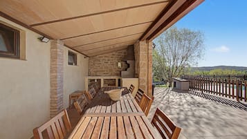 Un pati exterior amb taula i cadires de fusta, parets de pedra i vista del paisatge.