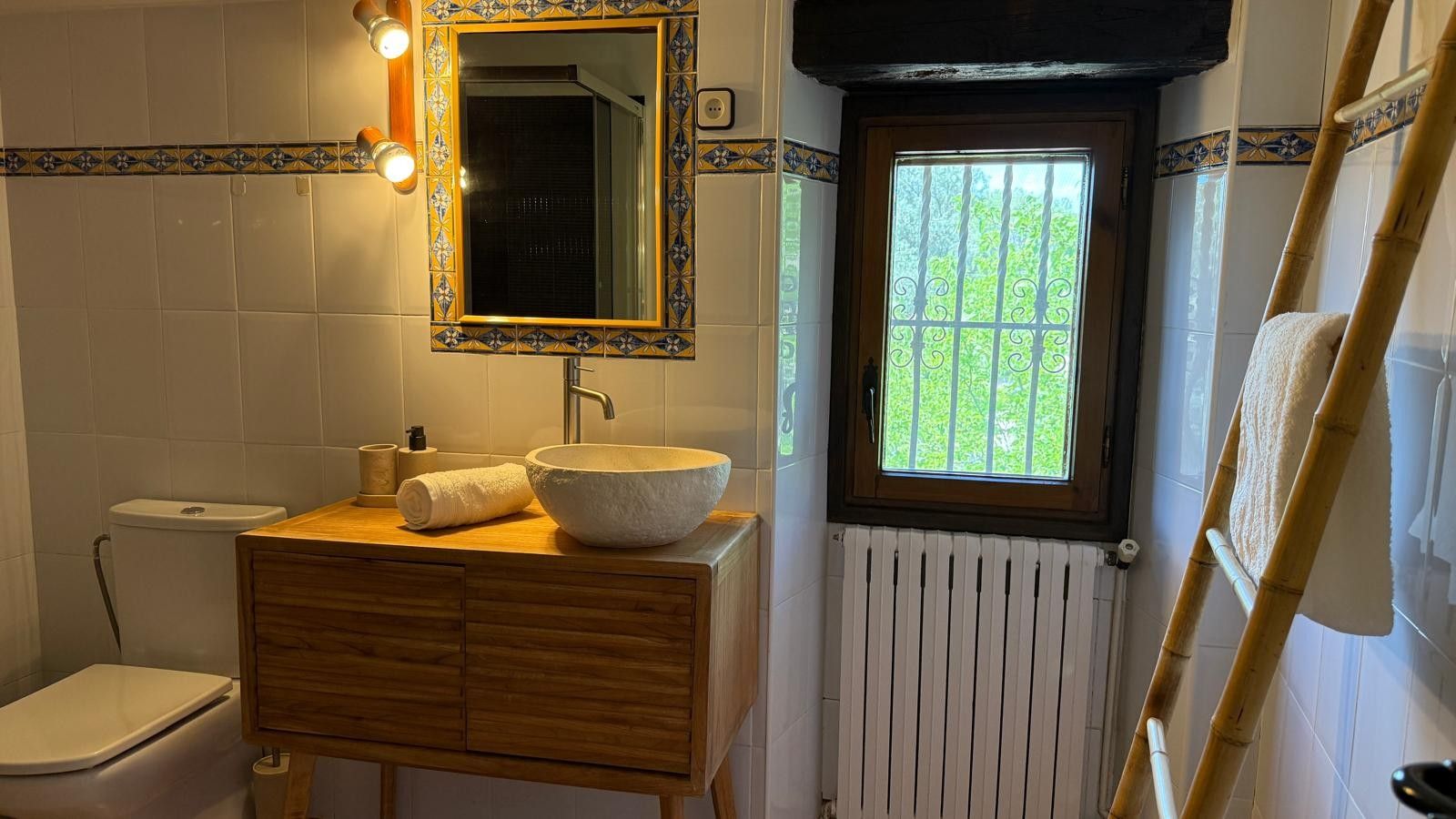Ein Badezimmer mit einem Holzkosmetikschrank, einem großen Waschbecken, einer Toilette und einem Fenster mit Blick auf Grünflächen.