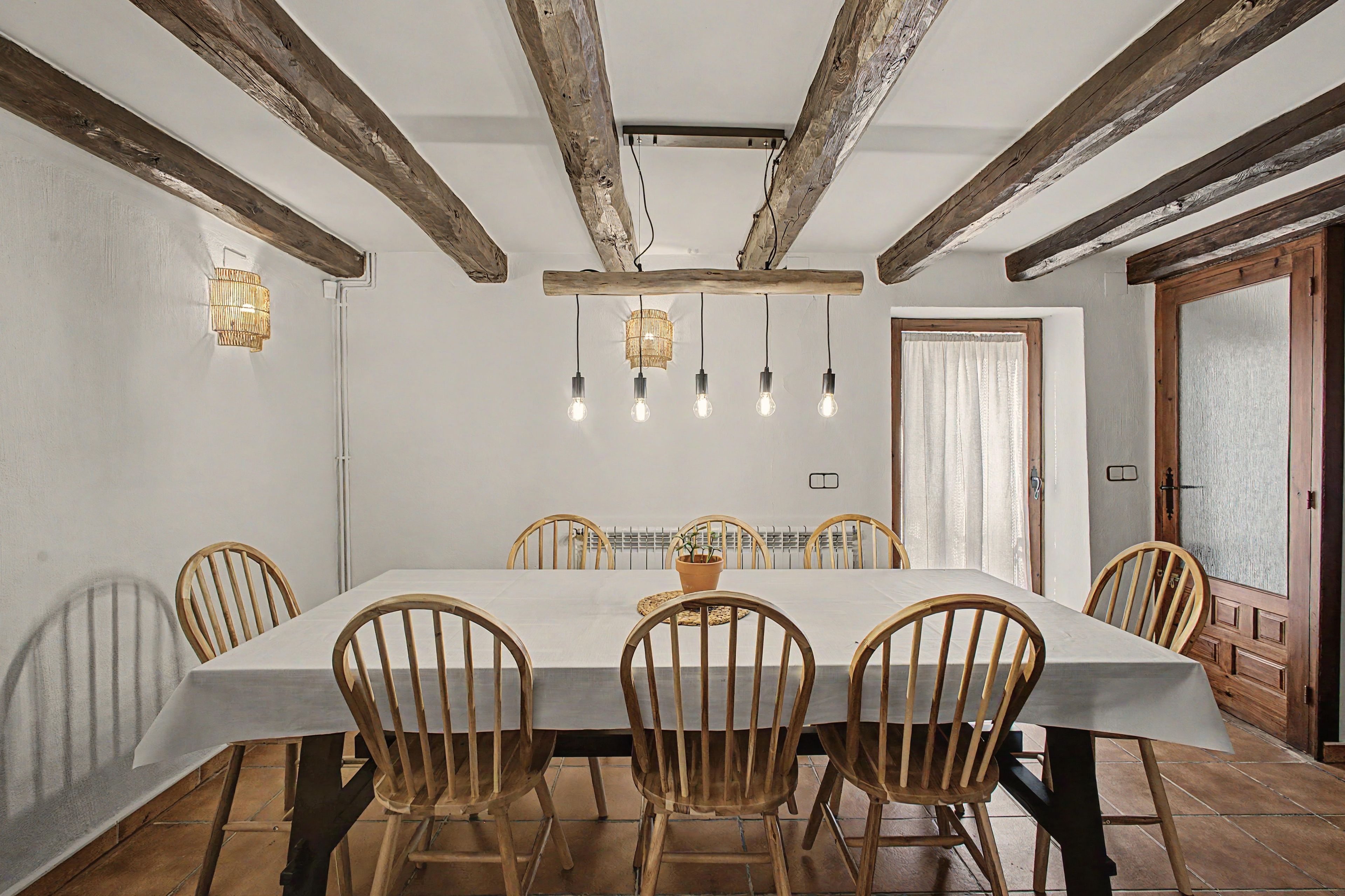A dining room with a long table, wooden chairs, and a rustic ceiling with exposed beams.