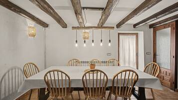 A dining room with a long table, wooden chairs, and a rustic ceiling with exposed beams.