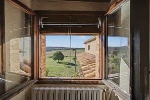 A room with a large window overlooking a rural landscape, including a tree and a building. - Country House 'El Casó Rural' with Private Pool in the Heart of Berguedà (Sorba - Montmajor)