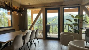 Ein Essbereich mit einem Holztisch, Stühlen, einer Chandelüster und Blick ins Freie.