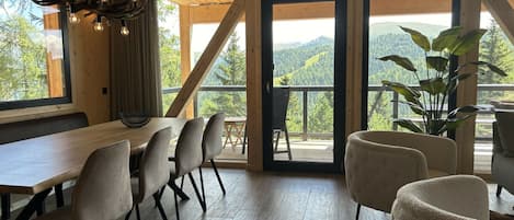 A dining area with a wooden table and chairs, a chandelier, and a view of the outdoors.