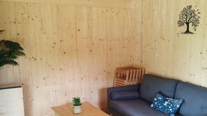 Ein Zimmer mit einer Holzwand, einem grauen Sofa, einem kleinen Holztisch mit einer Pflanze und einer Holzkiste.