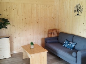 Een kamer met een houten wand, een grijze bank, een klein houten tafeltje met een plant en een houten kist.