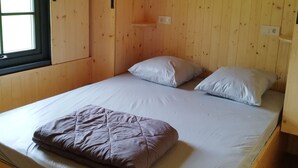 Ein Einzelbett mit weißer Matratze und zwei Kissen, ein Holz-Kopfbrett und ein Fenster mit Jalousien.