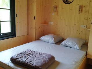 Een enkel bed met een witte matras en twee kussens, een houten hoofdbord en een raam met blinds.